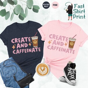May include: Two t-shirts with the text "Create and Caffeinate" and a cartoon coffee cup with a smiley face. The shirts are in heather navy and pink.