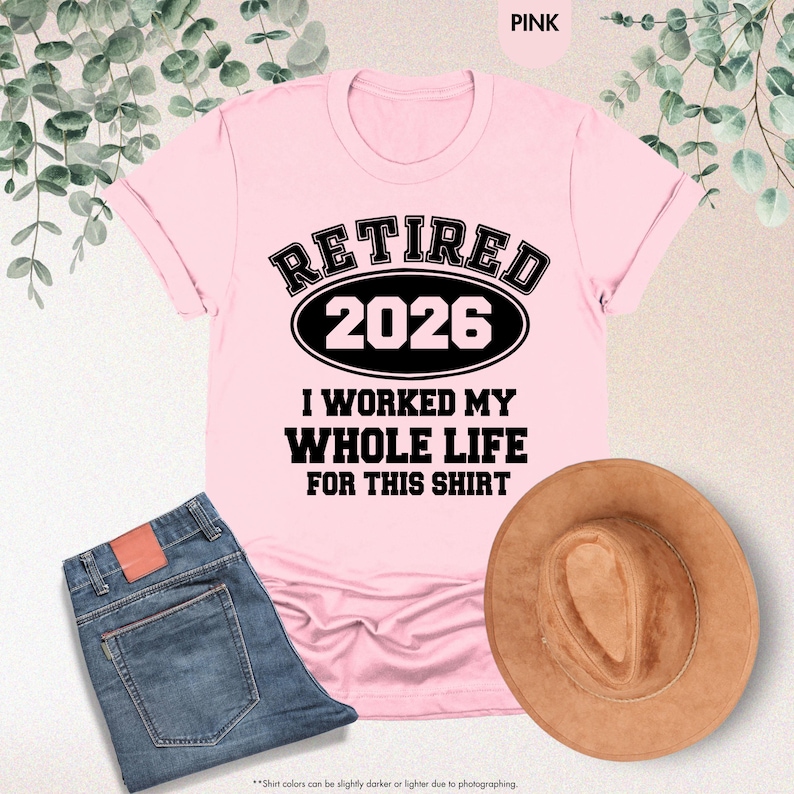 Puede incluir: Camiseta rosa claro con el texto negro "RETIRED 2026 I WORKED MY WHOLE LIFE FOR THIS SHIRT". La camiseta se combina con vaqueros azules y un sombrero marr&oacute;n. La palabra "PINK" est&aacute; en la esquina superior derecha.