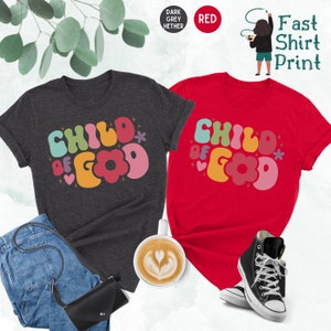 Op de afbeelding: Twee T-shirts met de tekst "Child of God" in kleurrijke, retro-stijl letters. De shirts zijn in donker grijs melange en rood.