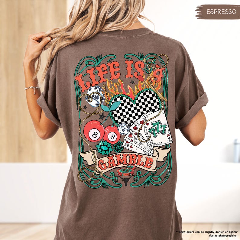 Puede incluir: Una camiseta marr&oacute;n con un estampado gr&aacute;fico de un coraz&oacute;n con un patr&oacute;n a cuadros, cerezas, dados, cartas de juego y el texto "Life is a Gamble".