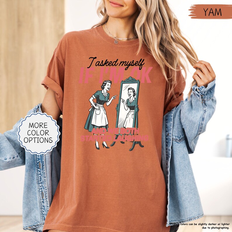 May include: A rust-colored t-shirt with the text "I asked myself if I look fat" and a retro illustration of a woman looking in a mirror. The shirt also has a graphic that says "and I said..." and "STILL FAT".