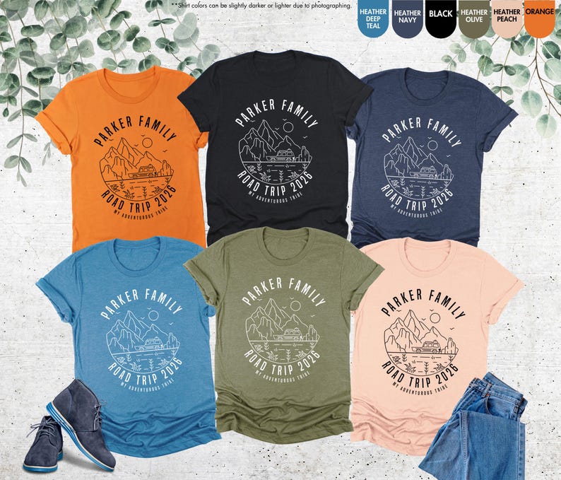 May include: Several t-shirts in shades like orange, black, and blue. Each shirt displays a white graphic with the text "PARKER FAMILY ROAD TRIP 2026" and a mountain and lake design. Some shirts are folded, and a pair of boots is visible.