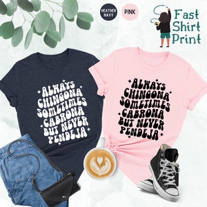 Puede incluir: Dos camisetas con un dise&ntilde;o de fuente retro. El texto en las camisetas dice "Always Chingona Sometimes Cabrona But Never Pendeja". Una camiseta es azul marino jaspeado y la otra es rosa.