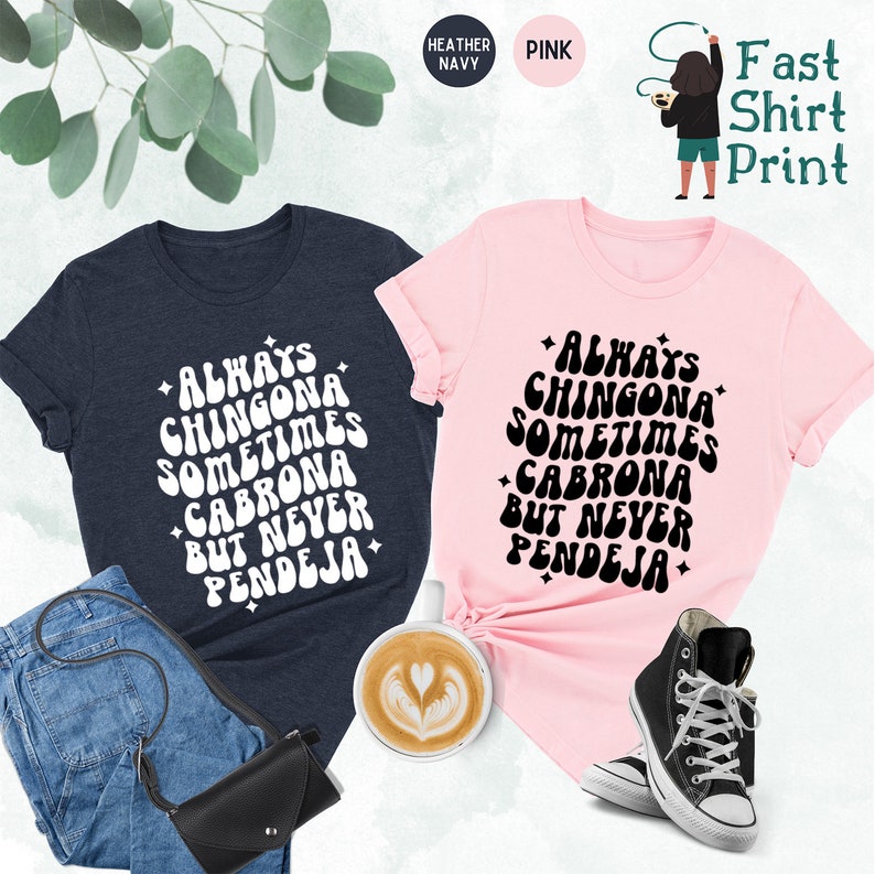 Puede incluir: Dos camisetas con un dise&ntilde;o de fuente retro. El texto en las camisetas dice "Always Chingona Sometimes Cabrona But Never Pendeja". Una camiseta es azul marino jaspeado y la otra es rosa.