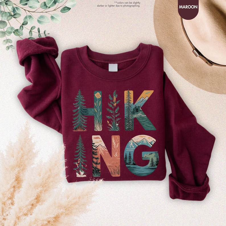 Pode incluir: Camisola de cor vinho com um design gr&aacute;fico da palavra "HIKING" com cenas da natureza incorporadas nas letras.