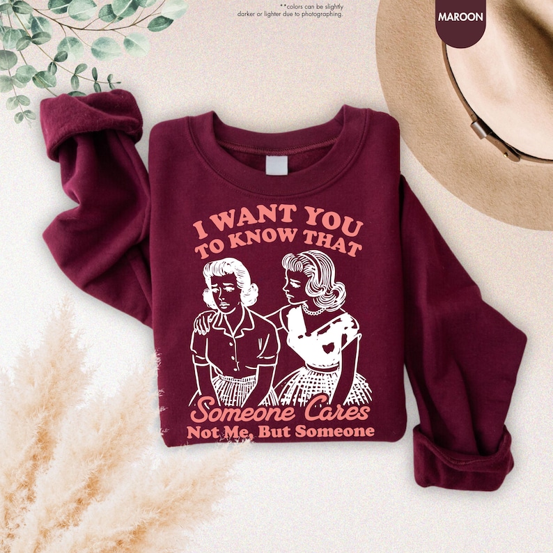 May include: Maroon sweatshirt with the text "I WANT YOU TO KNOW THAT Someone Cares Not Me, But Someone" and a graphic of two women. The sleeves are cuffed. The word "MAROON" is in the upper right corner.