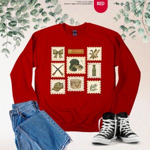 K&ouml;nnte beinhalten: Ein rotes Sweatshirt mit einer Reihe von Briefmarken im Jagd-Design. Die Briefmarken zeigen eine Schleife, einen Jagdhund mit einer Ente, gekreuzte Gewehre, einen Jagdhut, eine Holzkiste und andere jagdbezogene Bilder. Das Sweatshirt wird mit blauen Jeans und schwarzen Turnschuhen kombiniert.
