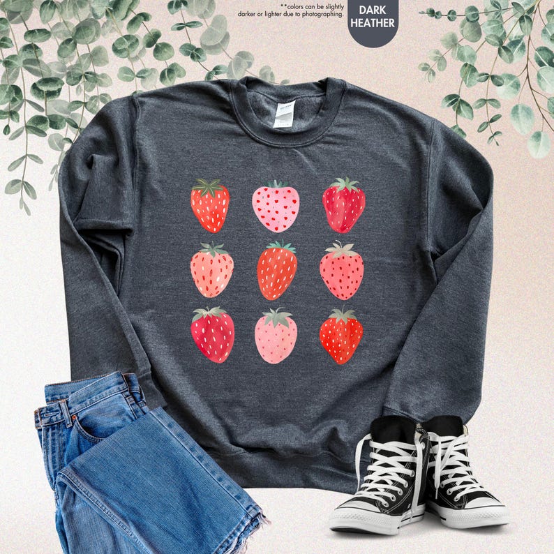 May include: A dark heather grey sweatshirt with a pattern of red and pink strawberries. The sweatshirt is shown on a model wearing blue jeans and black sneakers.
