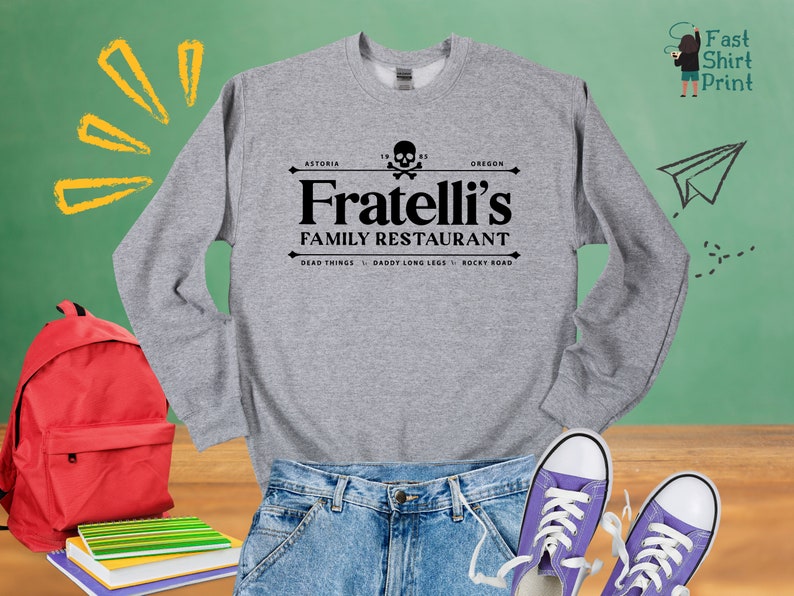 May include: A gray sweatshirt with a black graphic print of a skull and crossbones with the text "Fratelli's Family Restaurant" and the location "Astoria, Oregon". The text "Dead Things, Daddy Long Legs, Rocky Road" is printed below the restaurant name.