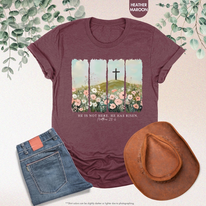May include: Heather maroon t-shirt with a floral design and a cross on a hill. The text "He is not here. He has risen. Matthew 28:6" is printed on the shirt.