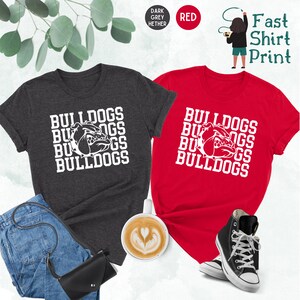 May include: Two t-shirts with the words "Bulldogs" and a bulldog head graphic printed on them. The shirts are in dark grey heather and red.