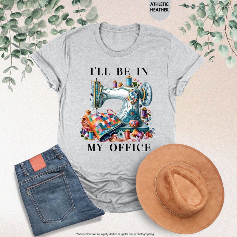Pode incluir: Uma camiseta cinza com o texto "I'll be in my office" e uma ilustra&ccedil;&atilde;o colorida de uma m&aacute;quina de costura com linha e tecido.