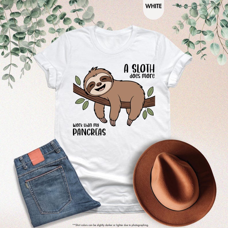 K&ouml;nnte beinhalten: Wei&szlig;es T-Shirt mit einem Cartoon-Faultier und dem Text "A SLOTH does more work than my PANCREAS". Das Bild zeigt blaue Jeans und einen braunen Hut.