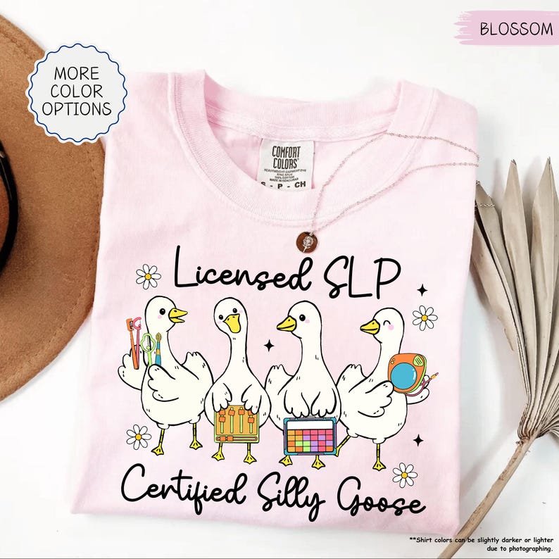 May include: A pale pink t-shirt featuring the words "Licensed SLP Certified Silly Goose" and a design of four cartoon geese with tools. The shirt has a round neck and short sleeves. The t-shirt is made of Comfort Colors material.