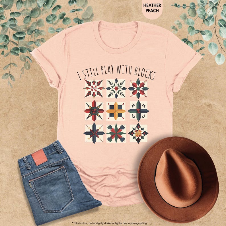 May include: A pink t-shirt with the text "I still play with blocks" and a design of colorful quilt blocks.