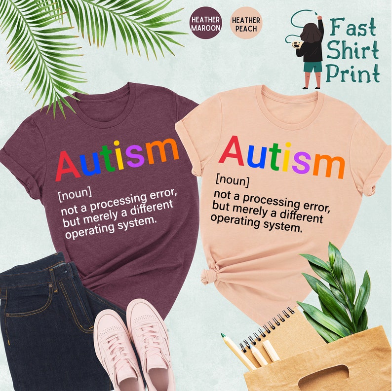 May include: Two t-shirts in heather maroon and heather peach colors with the word "Autism" printed in rainbow colors. The text below the word "Autism" reads "[noun] not a processing error, but merely a different operating system."
