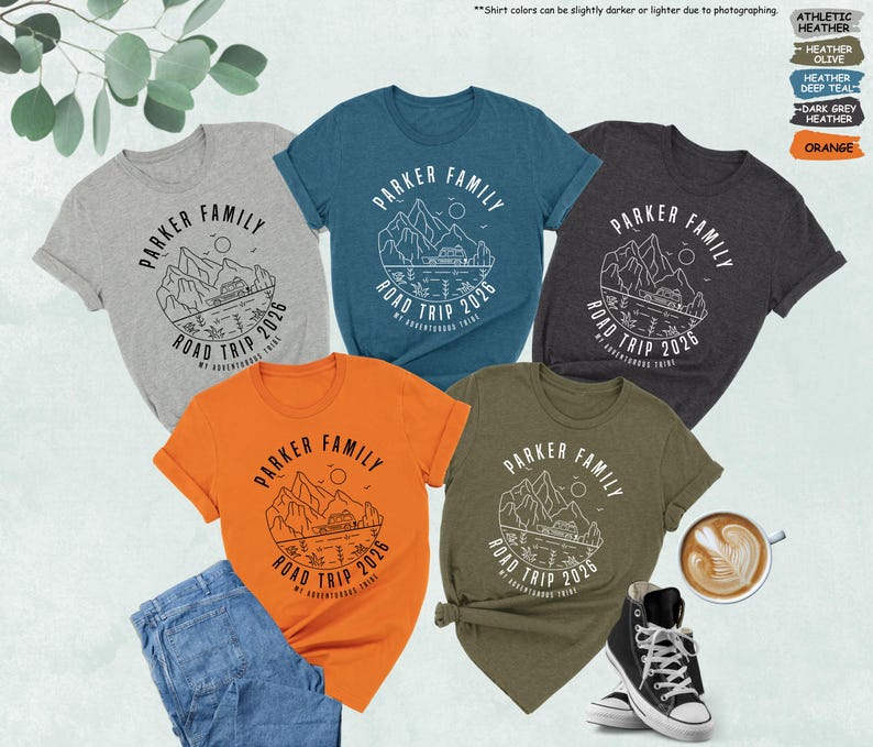 May include: Five short-sleeved t-shirts in heather grey, teal, dark grey, olive, and orange. Each shirt features a white graphic with the text "PARKER FAMILY ROAD TRIP 2026". The shirts are displayed with a pair of jeans, a cup of coffee, and a pair of black trainers.