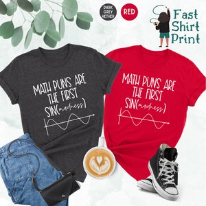 May include: Two t-shirts with the text "Math puns are the first sin(madness)" and a graph of a sine wave. The shirts are in dark heather grey and red.