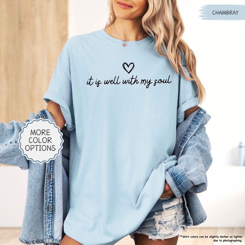 K&ouml;nnte beinhalten: Hellblaues T-Shirt mit dem handgeschriebenen Schriftzug "it is well with my soul" und einem kleinen Herz dar&uuml;ber. Das Shirt hat hochgekrempelte &Auml;rmel und ist aus weichem Stoff. Eine Jeansjacke ist ebenfalls im Bild zu sehen.
