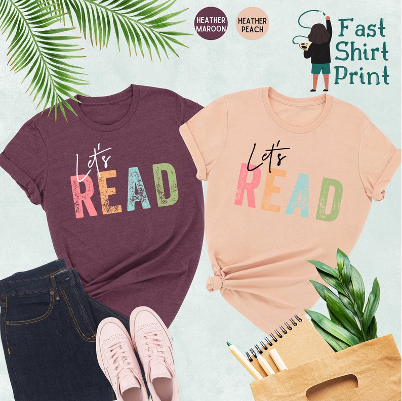 May include: Two t-shirts with the text "Let's Read" in colorful, distressed letters. The shirts are heather maroon and heather peach.