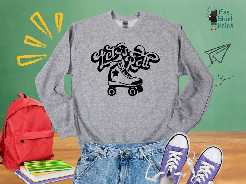 May include: A grey sweatshirt with the text "Let's Roll" in black, featuring a black and white roller skate graphic. The sweatshirt is displayed on a wooden surface with a red backpack, a pair of blue jeans, and two purple sneakers.