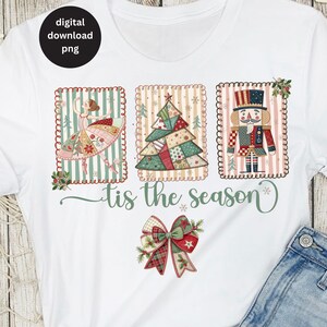 以下が含まれることがあります： バレリーナ、クリスマスツリー、くるみ割り人形をあしらったお祝いのデザインの白いTシャツ。「tis the season」の文字が筆記体で、装飾的なリボンが付いています。デジタルダウンロードPNGアイコンが左上にあります。
