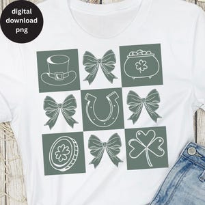 May include: A white t-shirt with a green square design featuring various Irish symbols, including a shamrock, a horseshoe, a pot of gold, a leprechaun hat, and bows.
