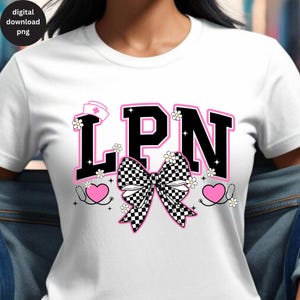 May include: White t-shirt with a graphic design featuring the letters "LPN" in black with a pink outline. A checkered bow, daisies, a nurse's hat, and stethoscopes complete the design.