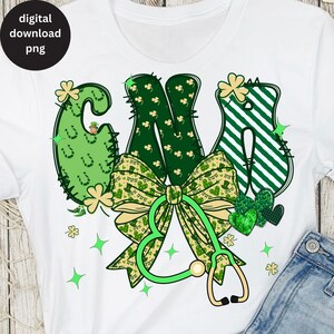 May include: White t-shirt featuring a green and gold design with the letters "CNS" in a festive St. Patrick's Day theme. The design includes shamrocks, a bow, and a stethoscope. The words "digital download png" are in a black circle in the upper left corner.