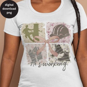 May include: A white t-shirt with a pink and brown collage design featuring a hard hat, work boots, gloves, and a silhouette of a person working on a utility pole. The text "He's working" is printed below the collage.