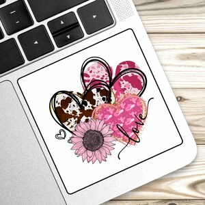 Puede incluir: Tres corazones rosas y marrones con una superposici&oacute;n de purpurina dorada y la palabra "love" escrita en cursiva. Un girasol rosa se encuentra debajo de los corazones.