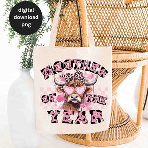 May include: A white tote bag with a pink and black cow graphic and the text "Moother of the Year".