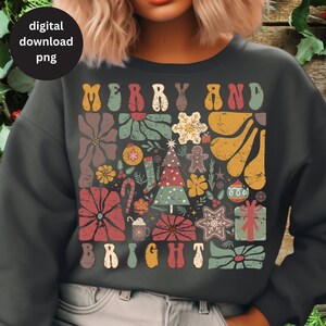 Op de afbeelding: Een donkergrijs sweatshirt met een retro-kerstontwerp. Het ontwerp bevat de woorden "Merry and Bright" in een kleurrijk, blokkerig lettertype, omringd door feestelijke afbeeldingen zoals een kerstboom, kerstversiering, snoepstokken en sneeuwvlokken.