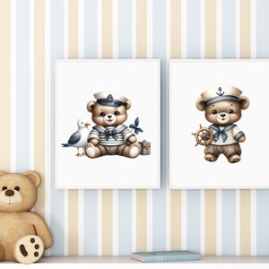 May include: Two framed prints featuring illustrations of teddy bears dressed as sailors. The bear on the left is holding a seagull and a suitcase. The bear on the right is holding a ship's wheel. Both bears are wearing blue and white striped sailor shirts and hats.