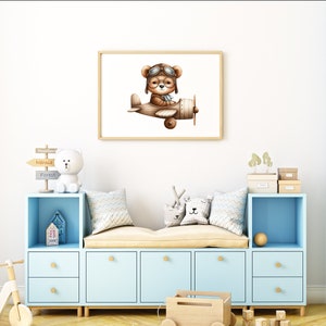 May include: A light blue toy storage bench with a brown cushion and a framed print of a brown bear wearing aviator goggles and flying a brown airplane. The print is on a white background. The bench has four drawers and two open shelves. There are various toys on the shelves, including a white stuffed bear, a wooden toy truck, and a wooden toy airplane.