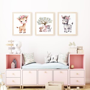 May include: Three framed watercolor illustrations of animals with floral headbands. The first illustration shows a giraffe, the second shows a tiger, a lion, and a zebra, and the third shows a zebra. The illustrations are hung on a white wall above a pink and white storage bench.