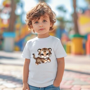 May include: A white t-shirt with a cartoon image of a cute tiger cub. The tiger is brown and orange with black stripes. The tiger is looking to the right and has a friendly expression.