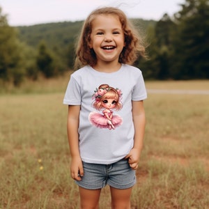 May include: A light blue t-shirt with a graphic of a cartoon ballerina wearing a pink tutu and a flower crown. The ballerina has brown hair and big blue eyes.