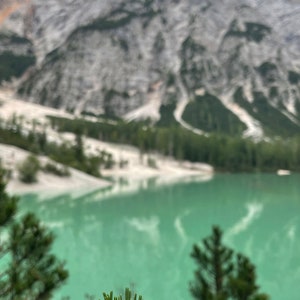 May include: A light blue gemstone bracelet on a pine tree branch with a mountain lake and mountains in the background.