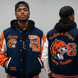 以下が含まれることがあります： 白袖のネイビーブルーとオレンジ色のスタジアムジャンパー。ジャケットには虎のロゴと前面に「Fineay」、背面に「Pruliom & Steiger」の文字が入っています。ジャケットの背面には「Pahiny Raoletta」の文字も入っています。