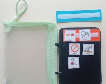 Puede incluir: Un estuche de malla verde claro con cremallera y asa, un tablero de comunicación rectangular negro con cinco tarjetas ilustradas cuadradas adheridas, y una tira azul separada con un cierre de velcro blanco. Las tarjetas muestran iconos.