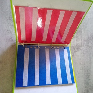 May include: An open binder with red and blue pages. The red page has white vertical stripes, and the blue page has white vertical stripes. The binder has a green border and metal rings.
