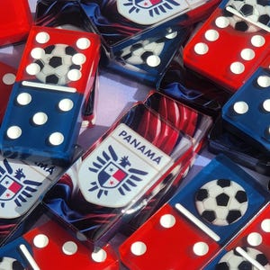 May include: A set of red and blue dominoes with white dots and football designs. The dominoes feature a Panamanian flag and the word "PANAMA" on some of the tiles.