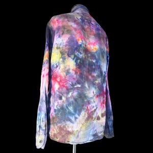 Może przedstawiać: Koszula z długim rękawem i zapięciem na guziki, ozdobiona żywym wzorem tie-dye w mieszanych odcieniach głębokiego fioletu, jasnego r&oacute;żu, ż&oacute;łci i ciemnego błękitu. Odzież posiada klasyczny kołnierzyk, mankiety na guziki oraz zapięcie na całej długości.