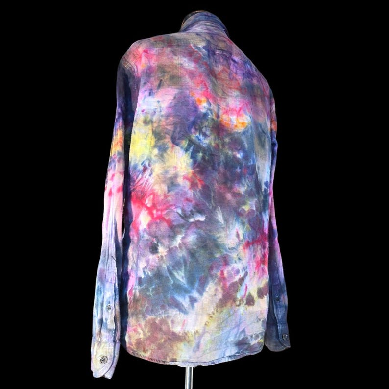 Może przedstawiać: Koszula z długim rękawem i zapięciem na guziki, ozdobiona żywym wzorem tie-dye w mieszanych odcieniach głębokiego fioletu, jasnego r&oacute;żu, ż&oacute;łci i ciemnego błękitu. Odzież posiada klasyczny kołnierzyk, mankiety na guziki oraz zapięcie na całej długości.