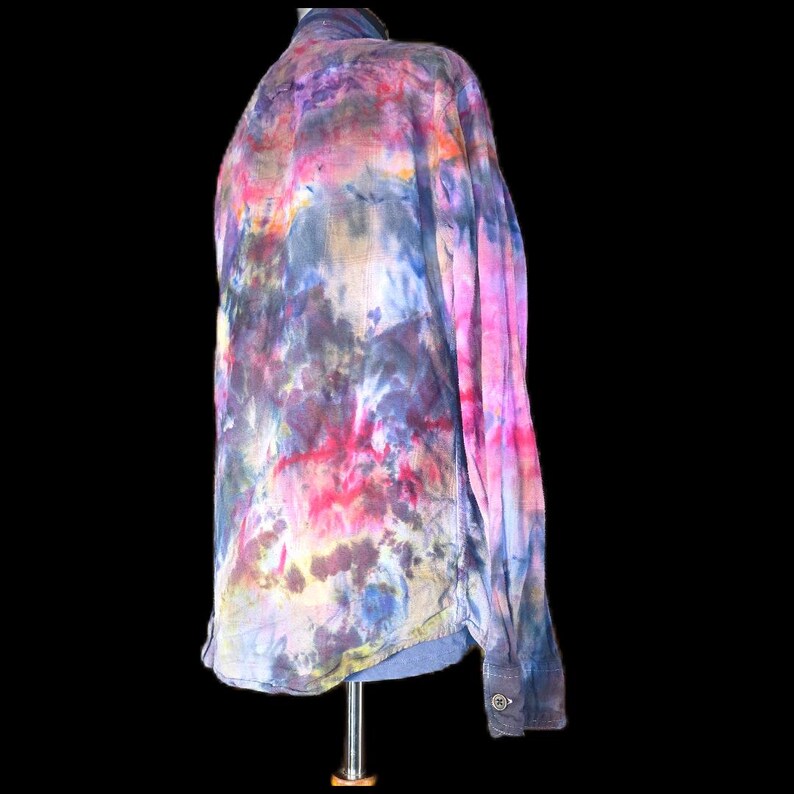 Może przedstawiać: Koszula z długim rękawem i zapięciem na guziki, ozdobiona żywym wzorem tie-dye w mieszanych odcieniach r&oacute;żu, fioletu, błękitu i ż&oacute;łci. Koszula posiada klasyczny kołnierzyk, przednią listwę guzikową oraz mankiety zapinane na guziki z marmurkowym efektem.