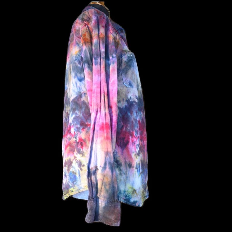 Może przedstawiać: Koszula z długim rękawem zapinana na guziki, ozdobiona żywym wzorem tie-dye w odcieniach r&oacute;żu, fioletu, błękitu i pomarańczu. Odzież posiada kołnierzyk, pojedynczą kieszeń na piersi po lewej stronie oraz mankiety zapinane na guziki.