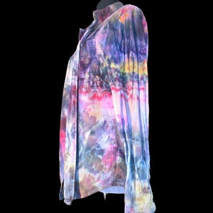 Może przedstawiać: Koszula z długim rękawem zapinana na guziki, ozdobiona żywym wzorem tie-dye z mieszanką odcieni fioletu, błękitu, r&oacute;żu i ż&oacute;łci. Koszula posiada klasyczny kołnierzyk, przednią listwę z guzikami oraz pojedynczą kieszeń na piersi po lewej stronie.