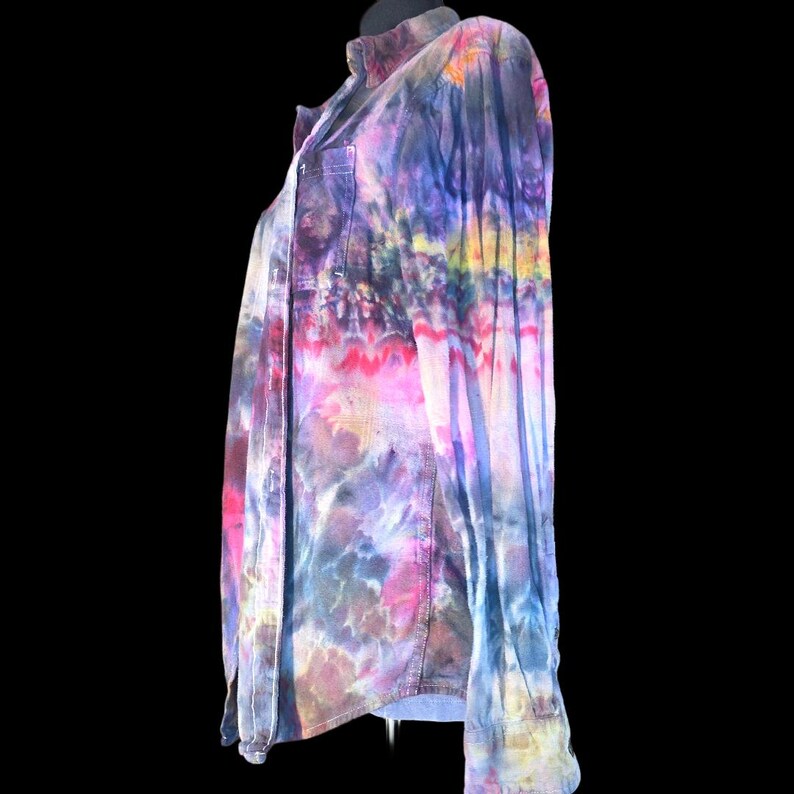 Może przedstawiać: Koszula z długim rękawem zapinana na guziki, ozdobiona żywym wzorem tie-dye z mieszanką odcieni fioletu, błękitu, r&oacute;żu i ż&oacute;łci. Koszula posiada klasyczny kołnierzyk, przednią listwę z guzikami oraz pojedynczą kieszeń na piersi po lewej stronie.