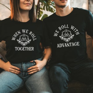 May include: A couple wearing matching black t-shirts with a white graphic of a twenty-sided die. The woman's shirt says "When we roll together" and the man's shirt says "We roll with advantage".
